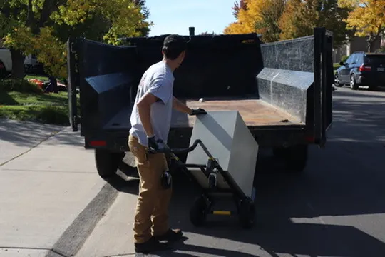 Ben from EZ Haulaway loading a cabinet on a dolly into the black dump trailer